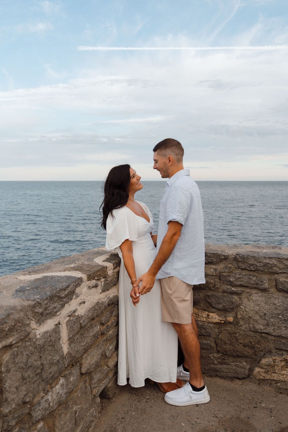 A couple shares a tender moment at a scenic ocean overlook with blue skies and rocky cliffs.