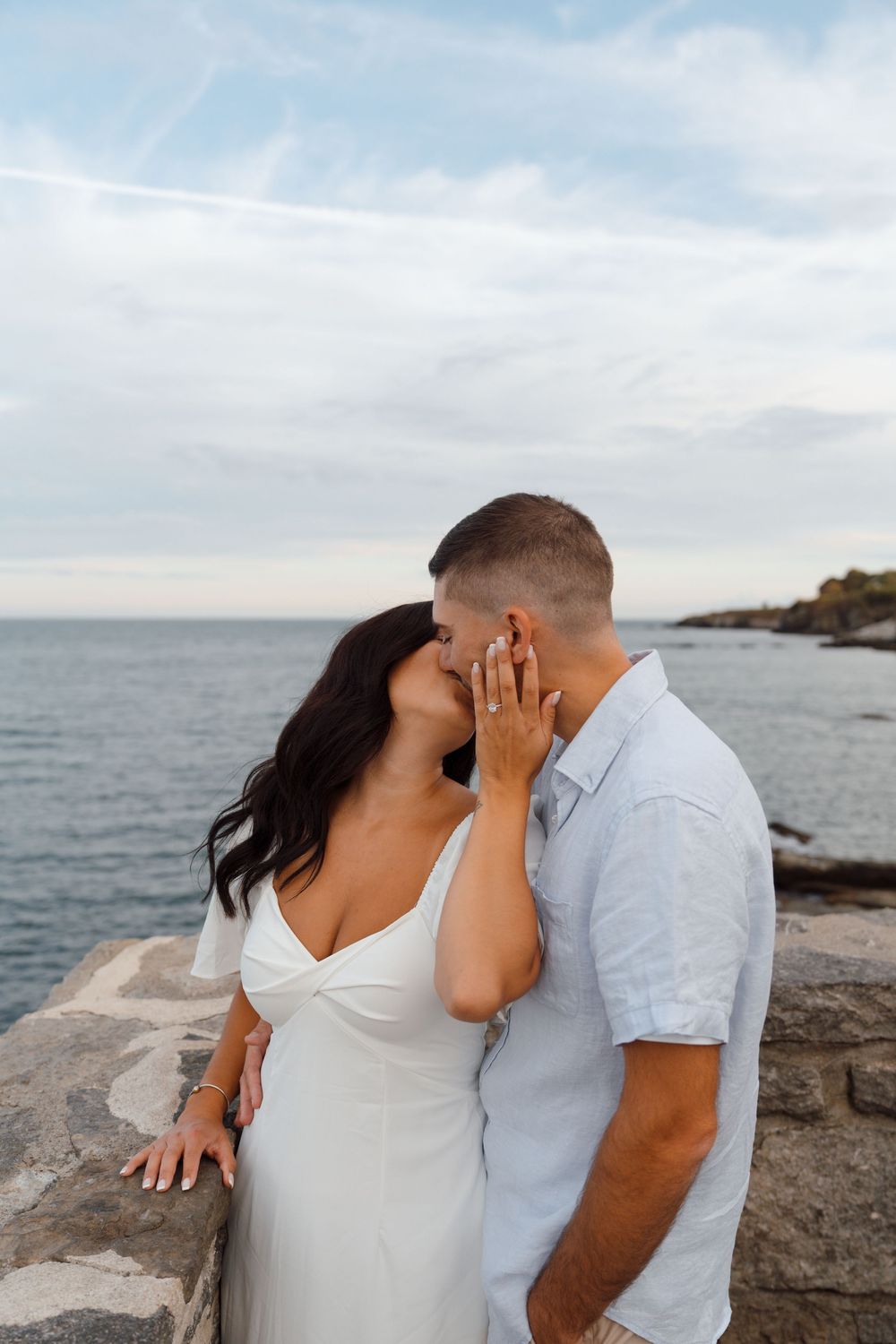A romantic couple shares intimate moments by the ocean while posing for a series of engagement photos at the coastline.