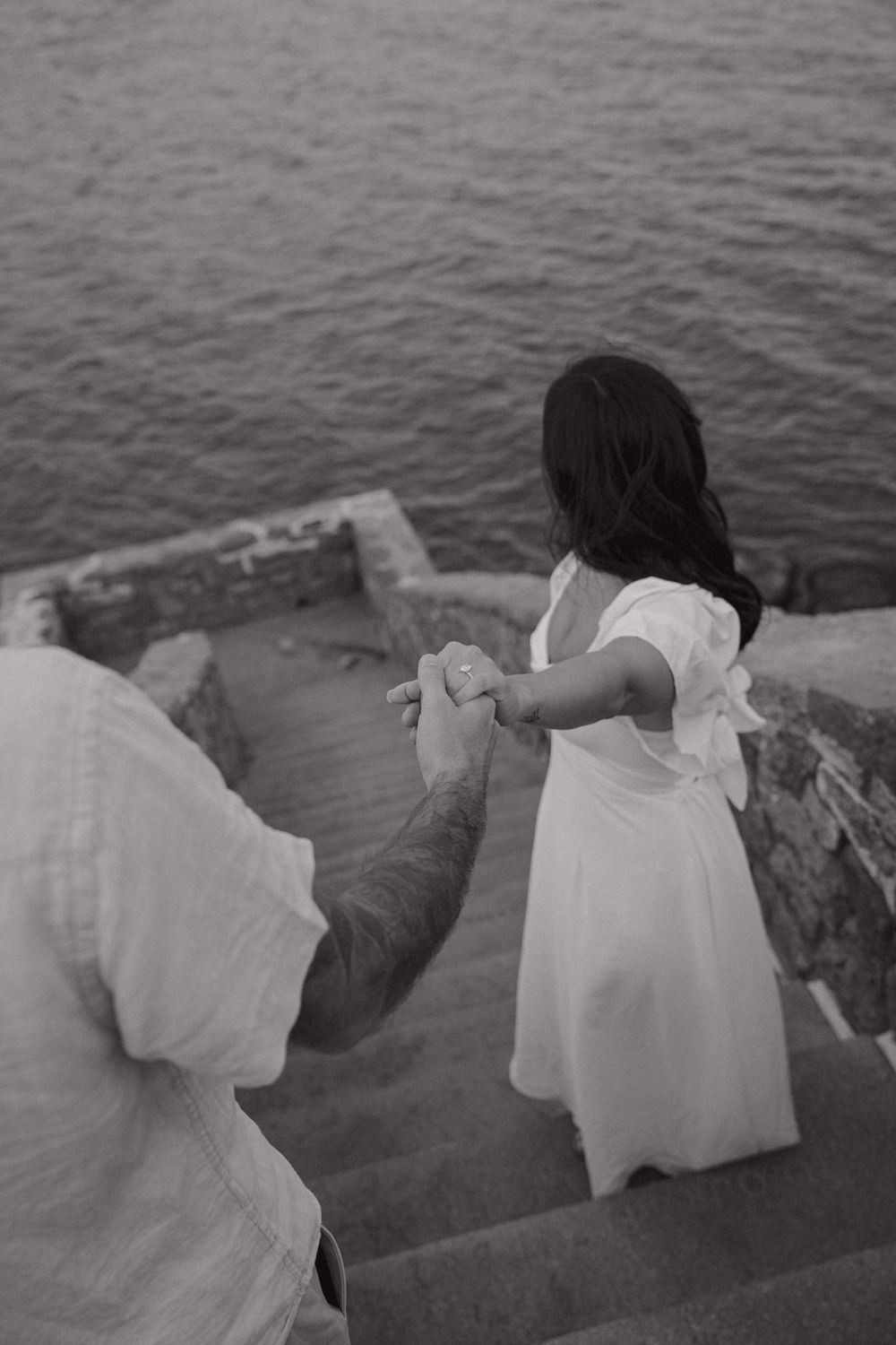 Two people in white clothes sitting close together on stone steps by the water.