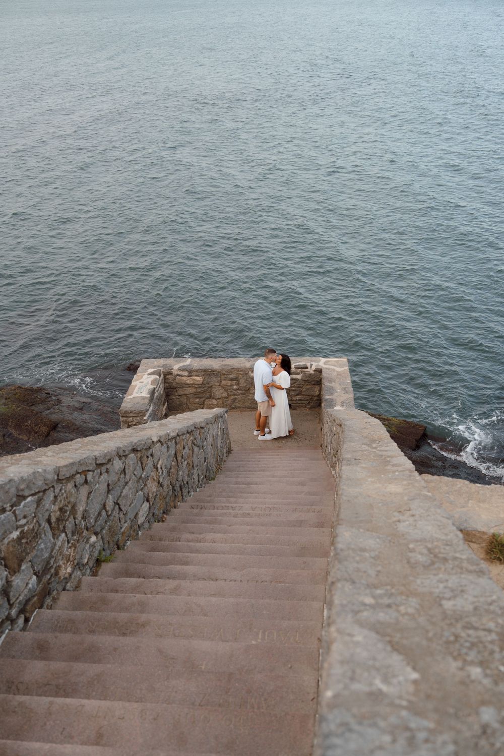 Stone stairs descend to the ocean with rocky walls on each side leading to a scenic coastal viewpoint.