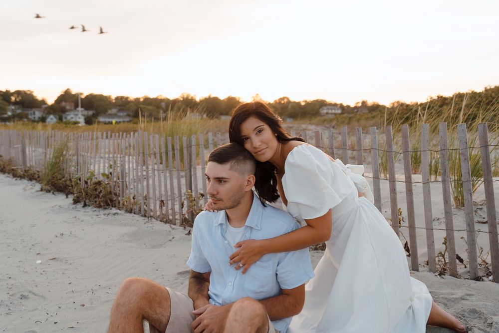 A couple in white outfits enjoying a romantic moment on a sandy beach with wooden fences.