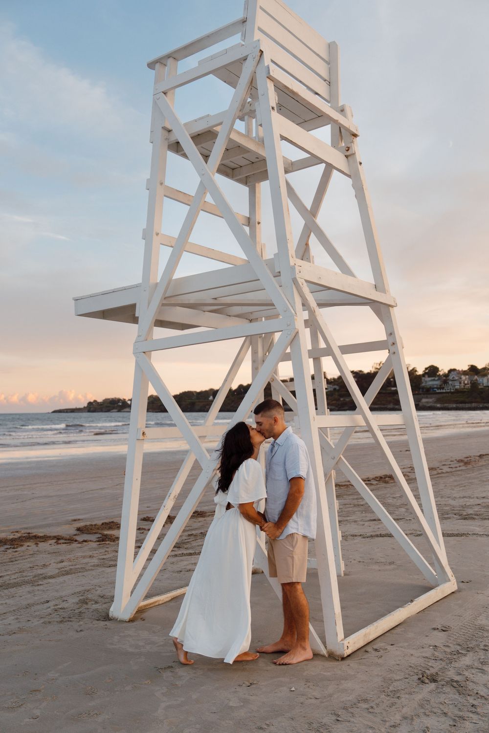 Beach photoshoot with white lifeguard chair on sandy shore at sunset.