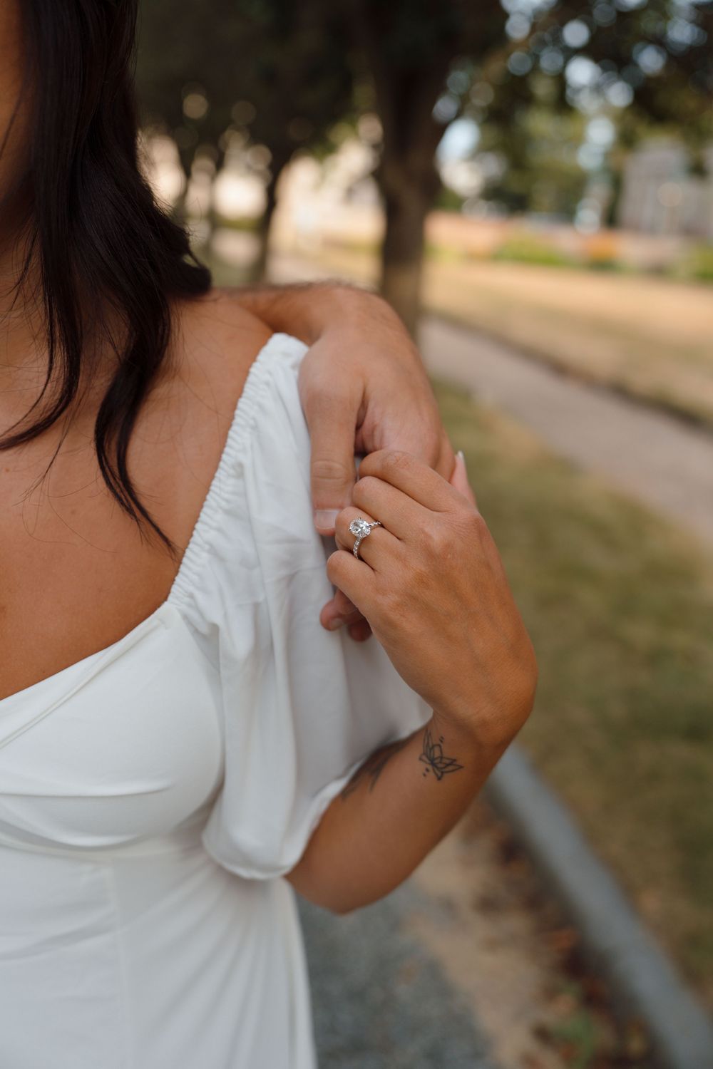 A close-up view of a white sleeve and arm with a small tattoo detail against a blurred outdoor background.