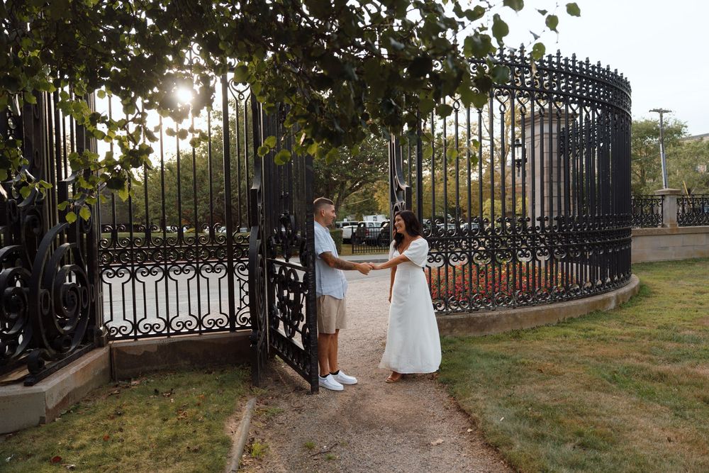 A couple posing by an ornate black iron gate on a garden path during sunset.