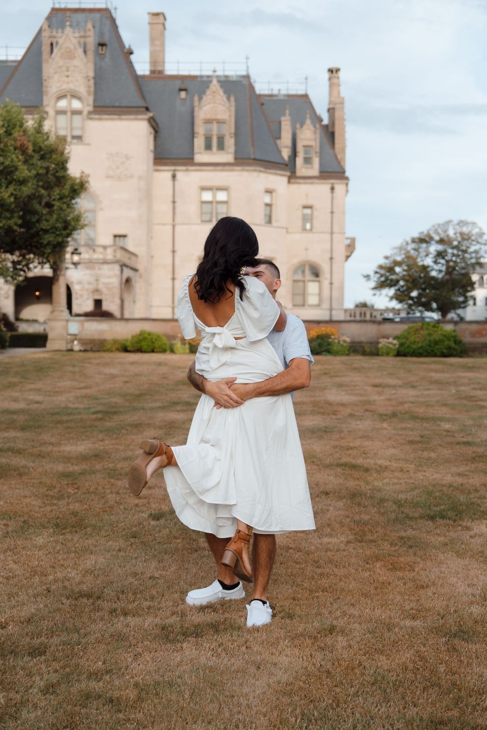 A romantic photoshoot on a grassy lawn with a majestic mansion visible in the background.