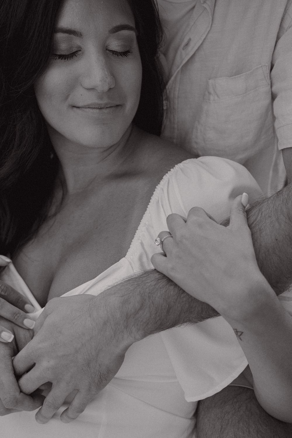 An intimate black and white close-up portrait showing tender embracing hands and flowing fabric.