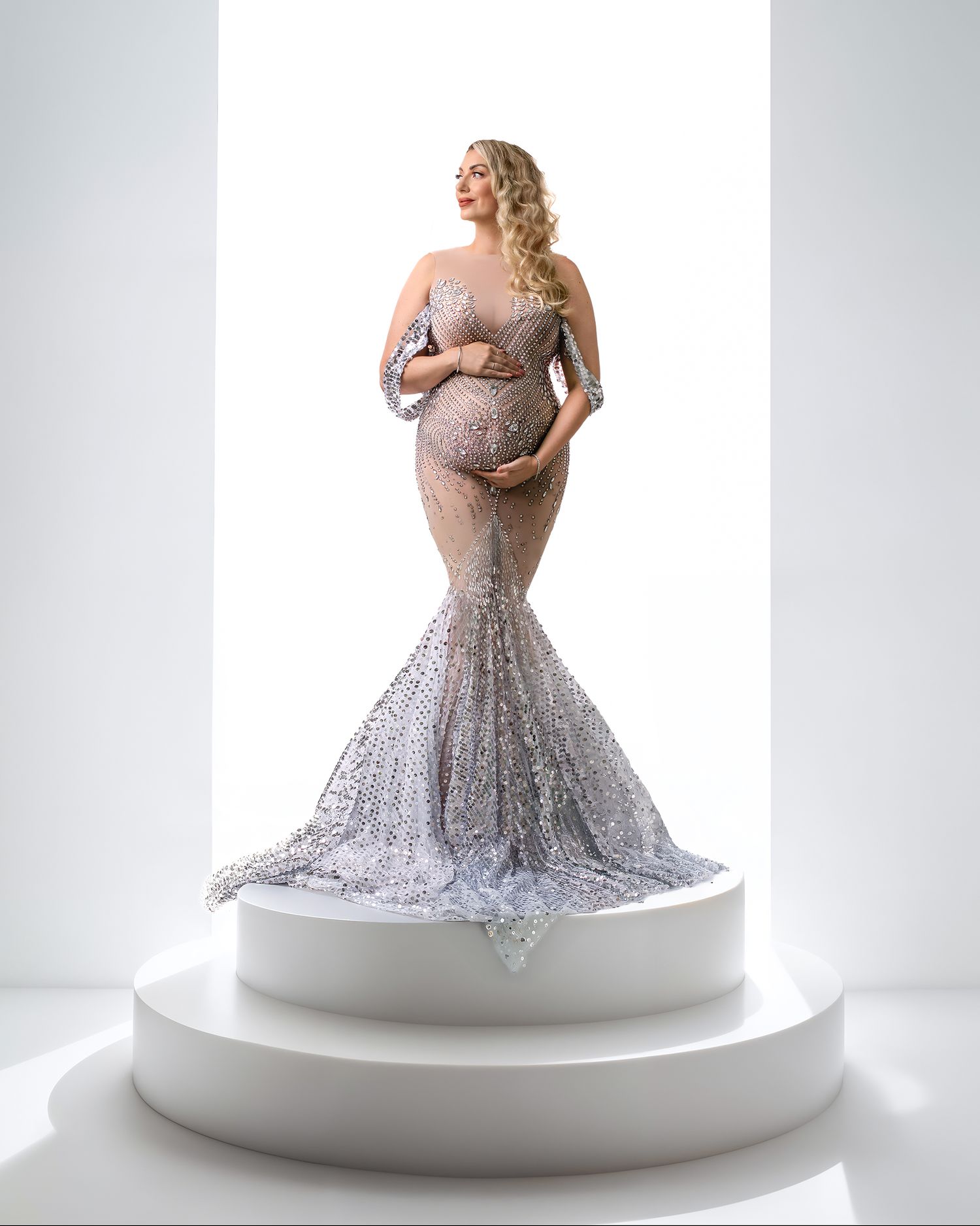 Woman in a silver sequin gown, elegant standing pose, on a posing block, backlit, full body studio shot.