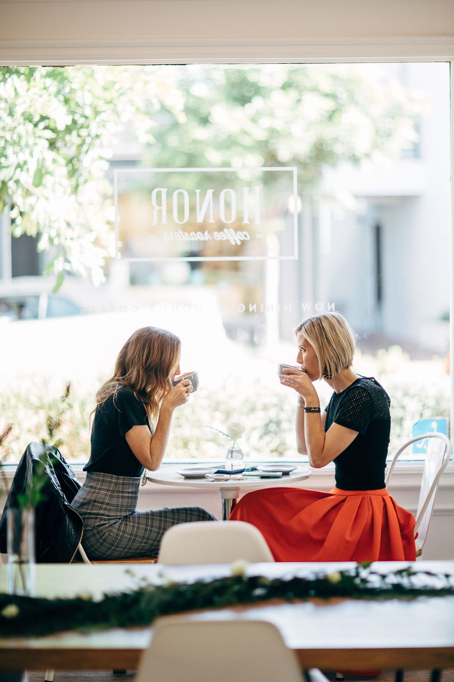 Women lounging and chatting by window in casual cafe setting.
