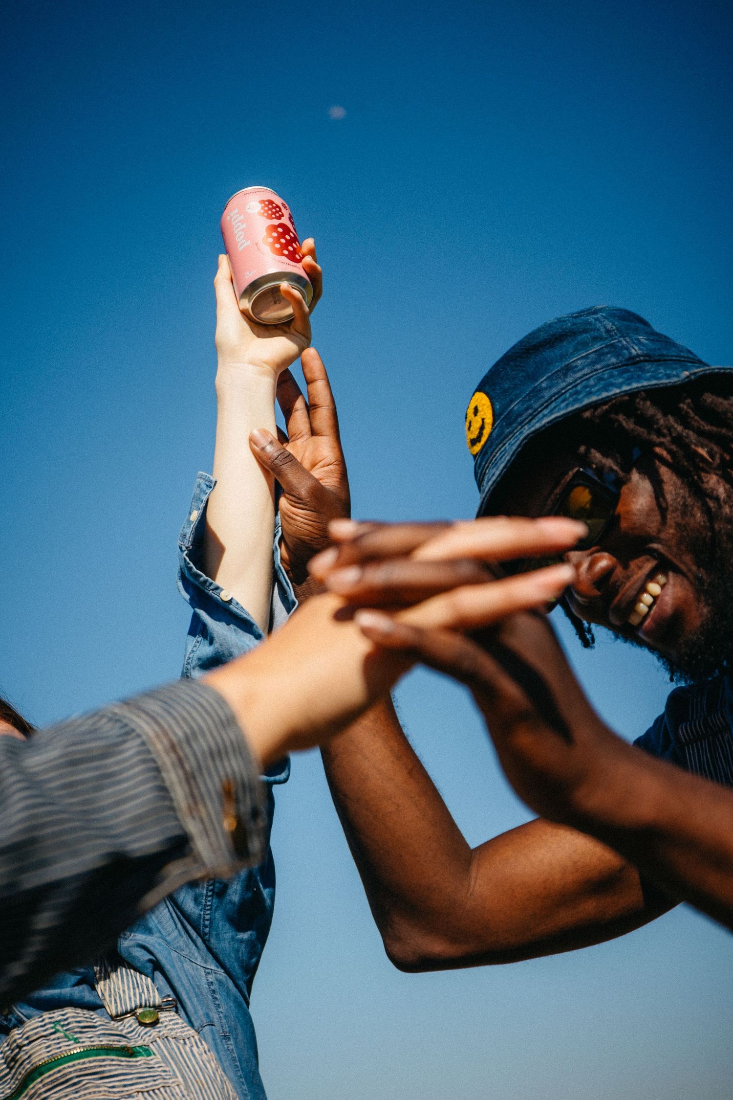 Two hands toasting drinks against a blue sky background.