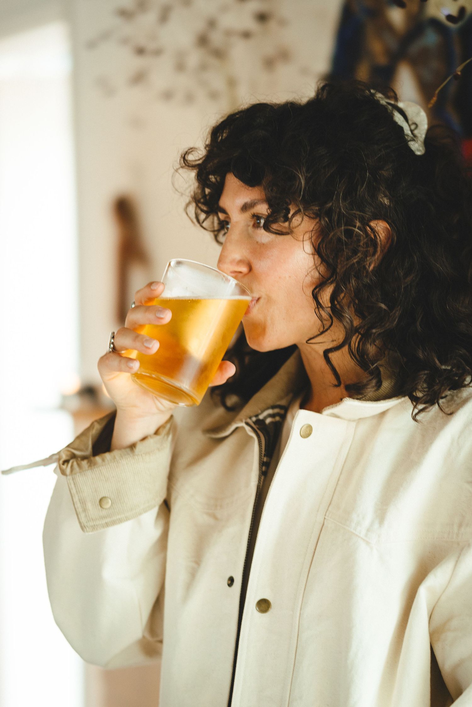Person in white jacket enjoying a glass of golden beer in a series of progressive drinking shots.