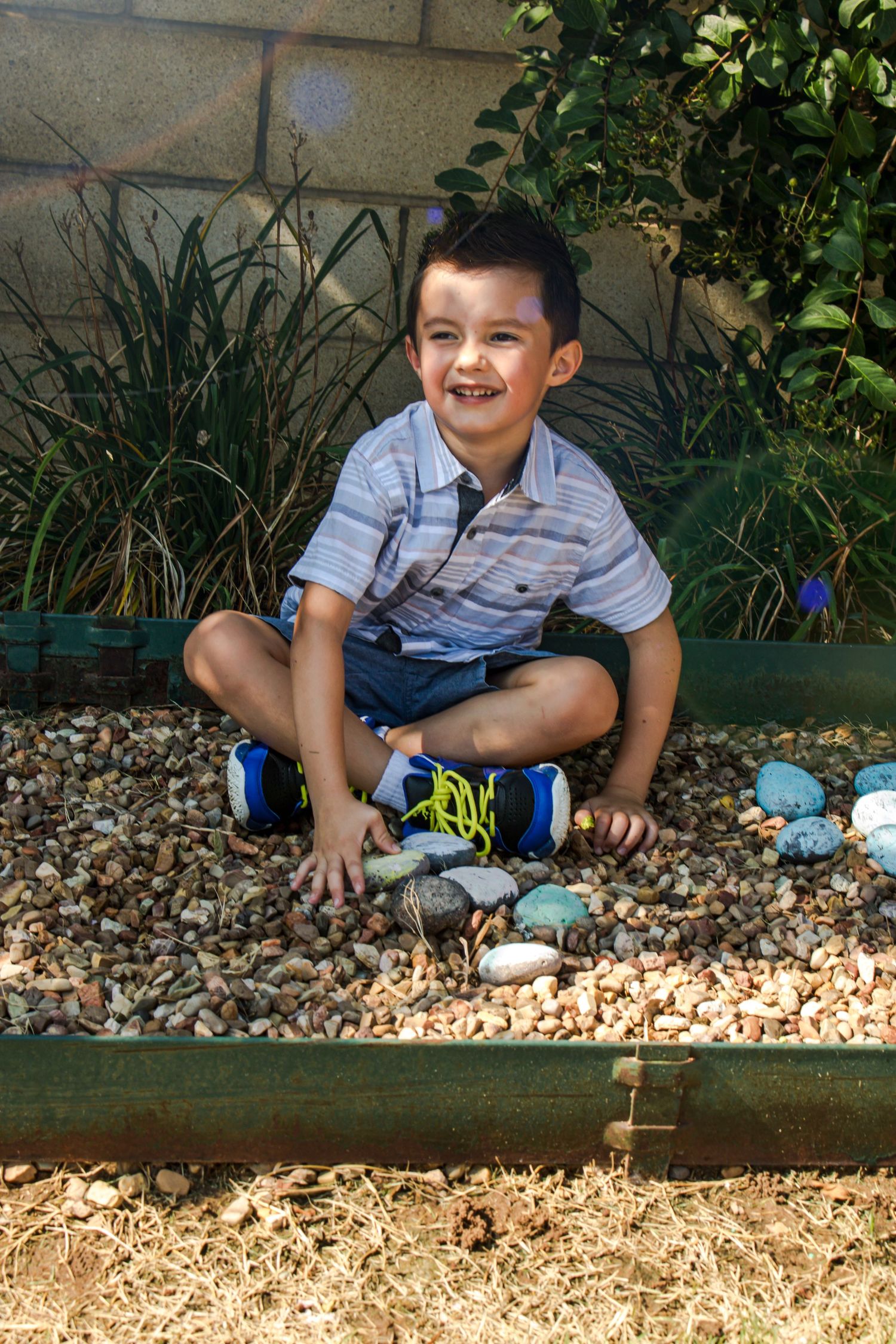 A child sits playfully on grey stone landscaping rocks near a garden wall.