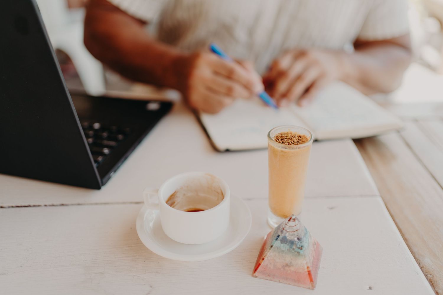 People working at desks in modern office with coffee cups, laptops and notebooks in collaborative workspace setting.