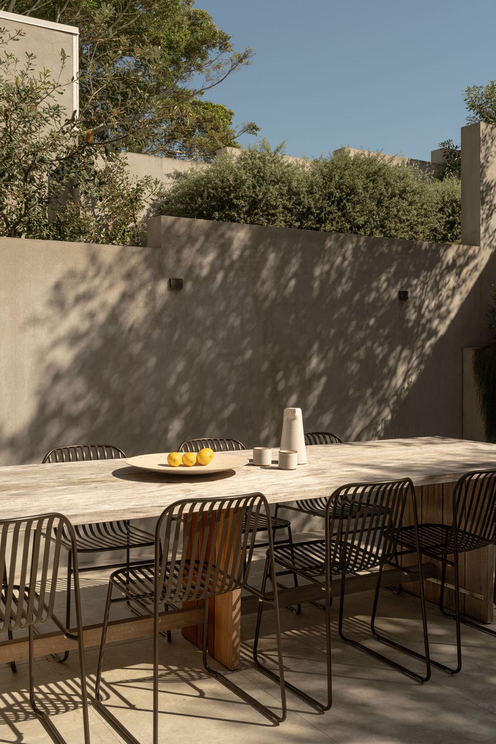 Modern outdoor seating area with sleek black chairs arranged along a white wall in natural sunlight.