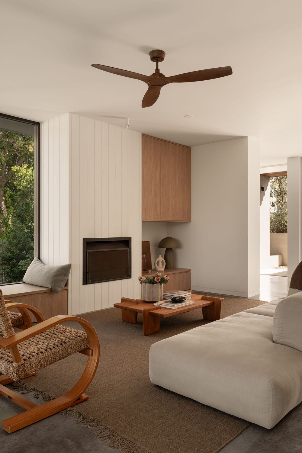 Contemporary living space featuring wooden furniture, ceiling fan, and white sectional sofa on brown carpet.
