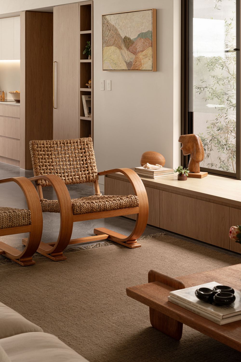 Minimalist living room with curved wooden chairs and patterned cushions against white walls and built-in storage.
