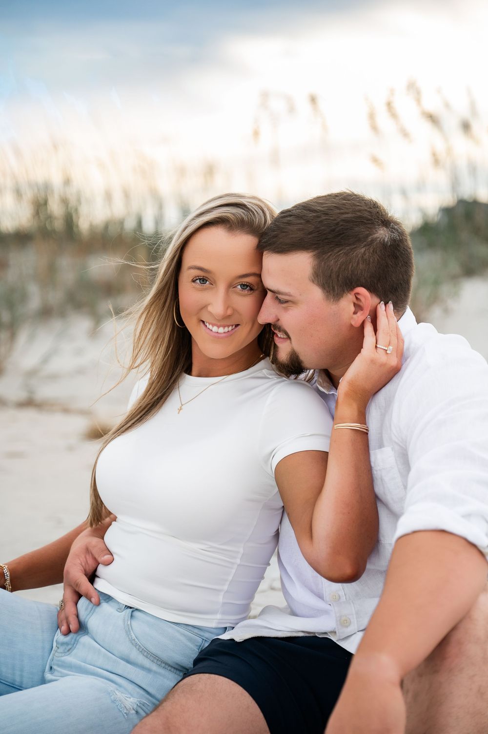 Couple sitting on beach dunes during golden hour photography session.