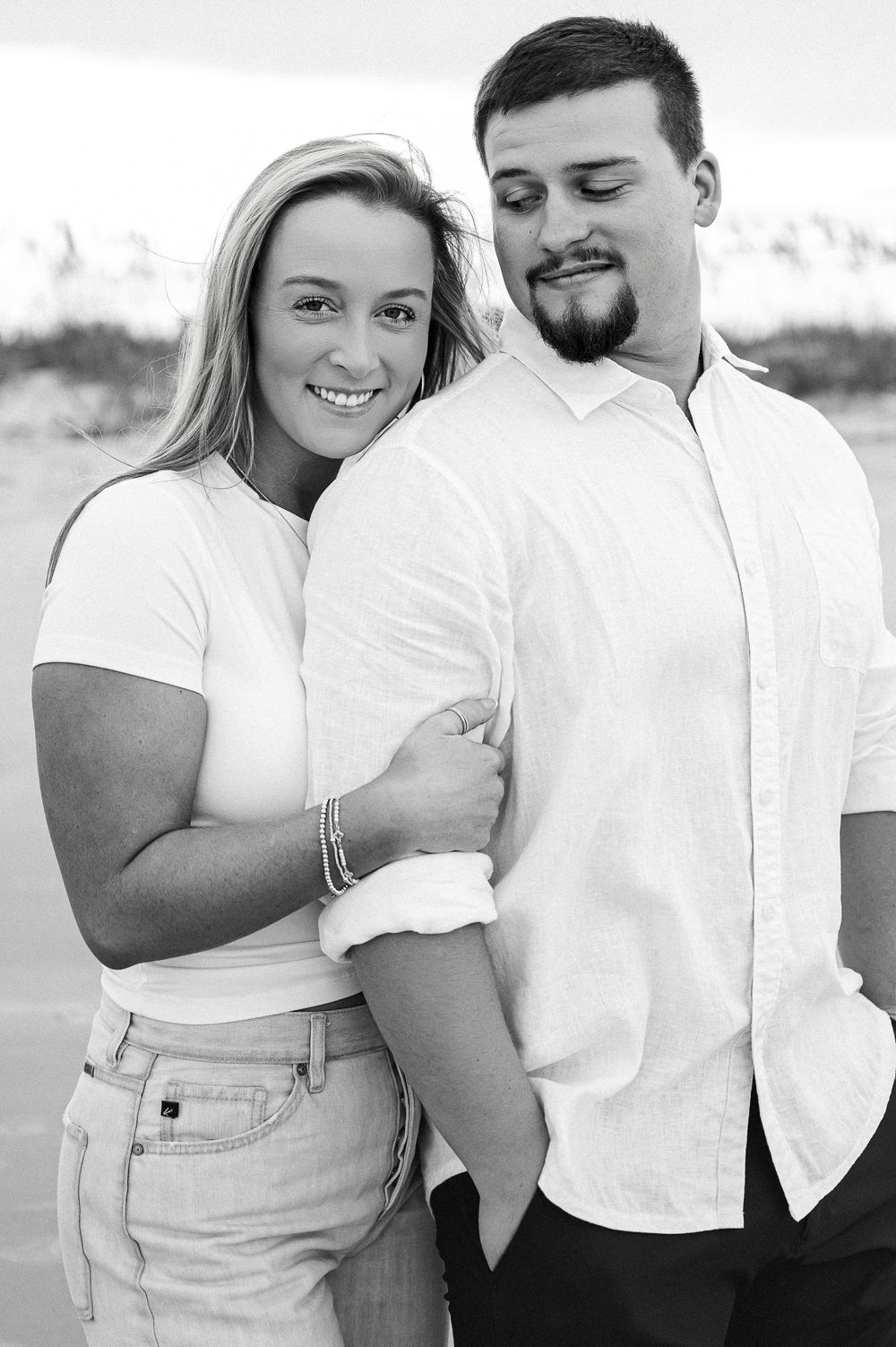Black and white portrait of couple in casual attire on beach.