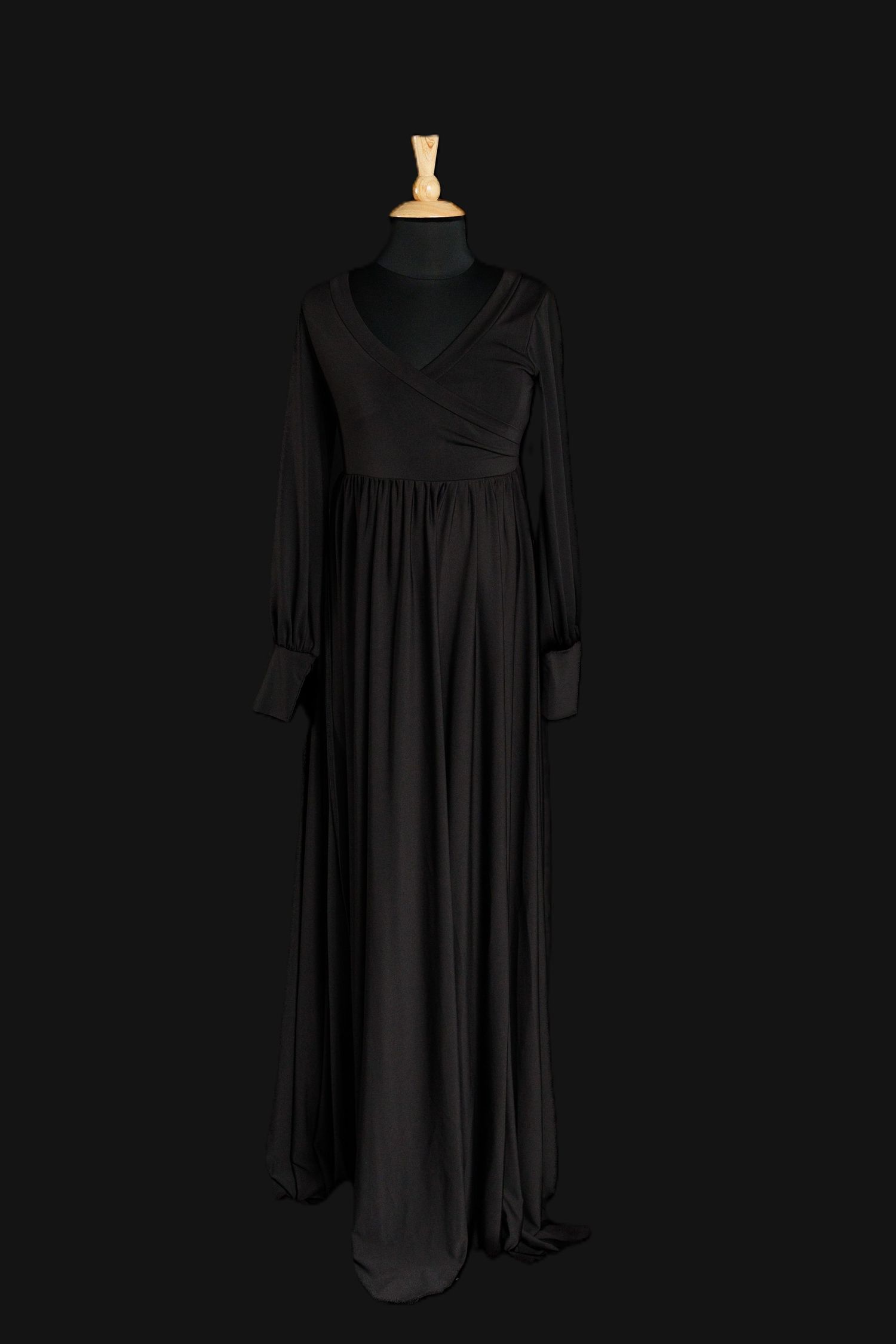 Black long-sleeve maternity gown with wrap-style V neckline, empire waist, and full flowing skirt on a dress form.