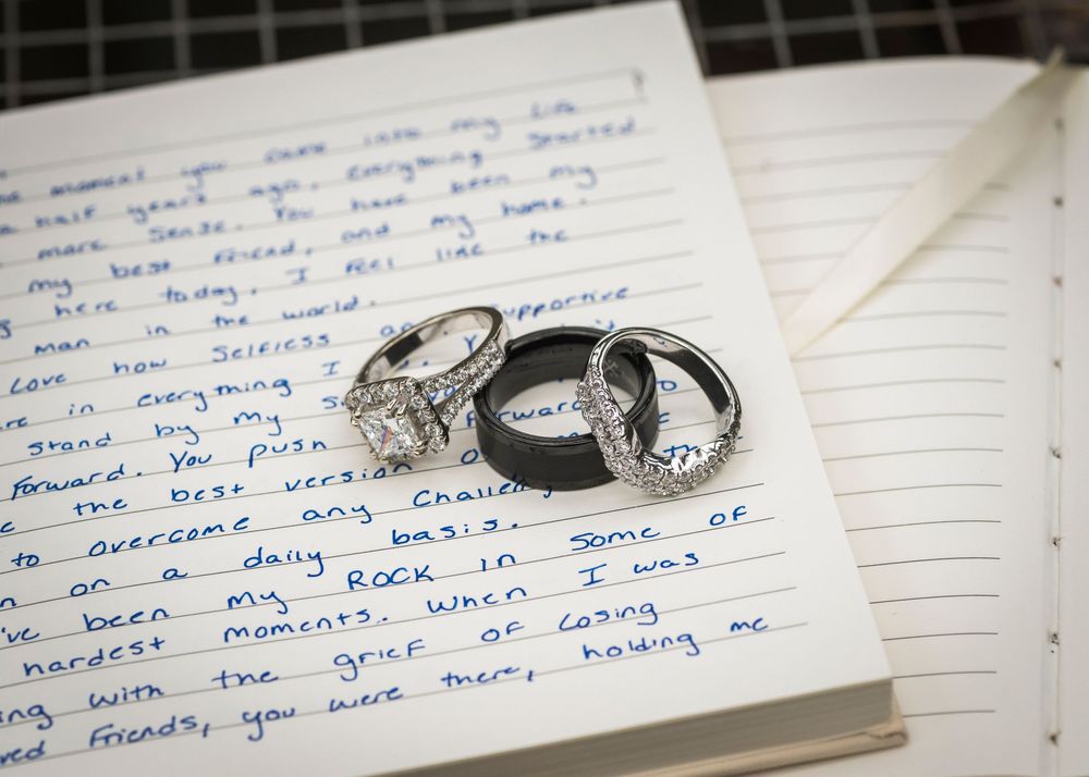 Three wedding rings rest on open journal with handwritten love letter in cursive ink.
