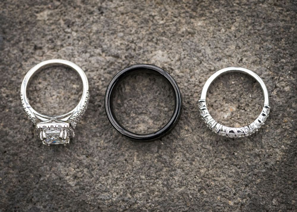 Three wedding rings on stone surface, including diamond engagement ring and black tungsten band.