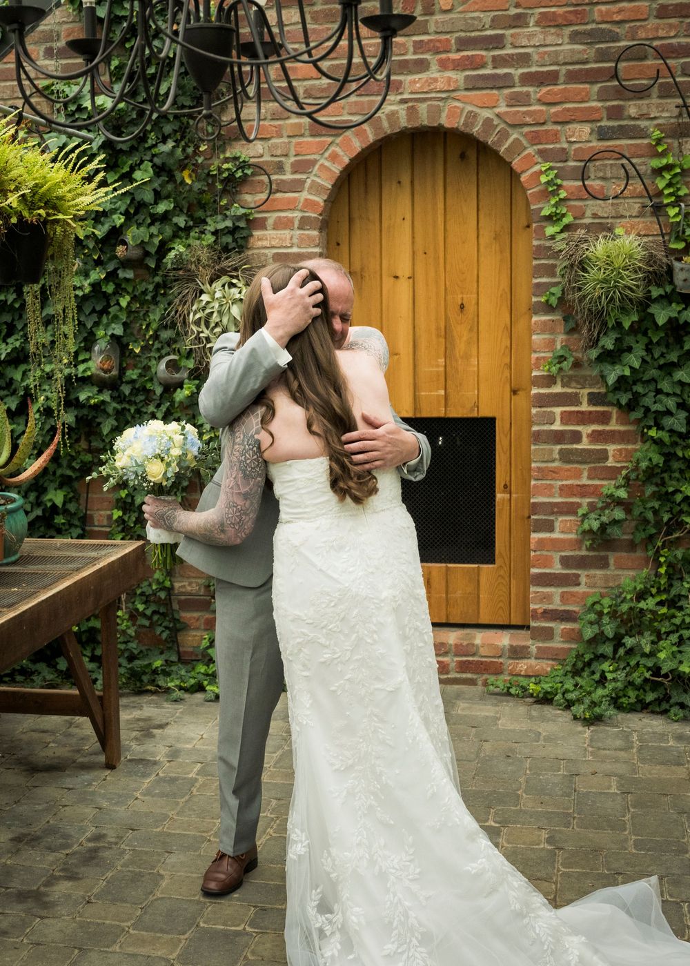 Bride and groom share a romantic kiss in a brick courtyard with ivy walls and wooden arched door.