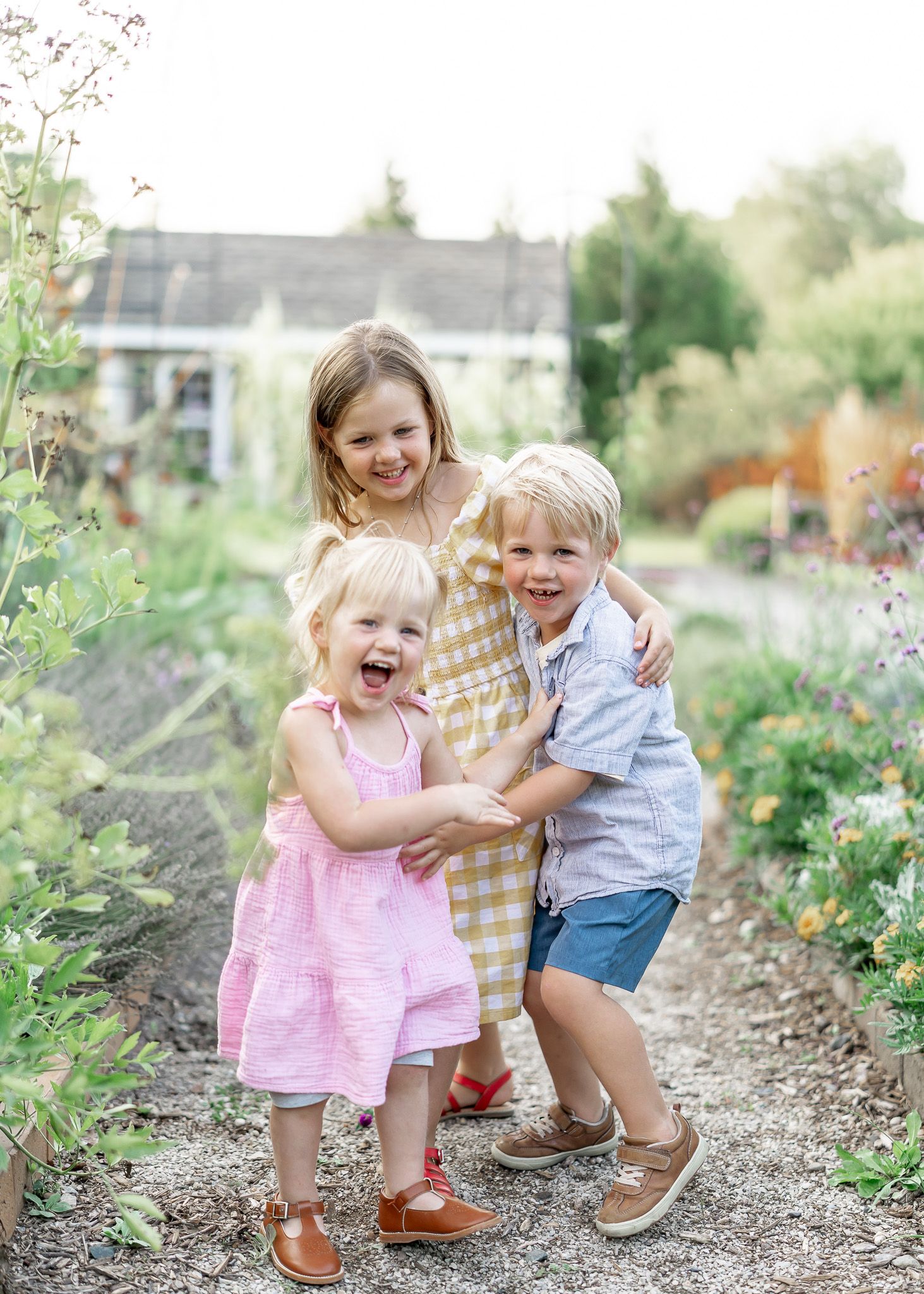 Children playing and laughing together in a garden path surrounded by blooming flowers and greenery.
