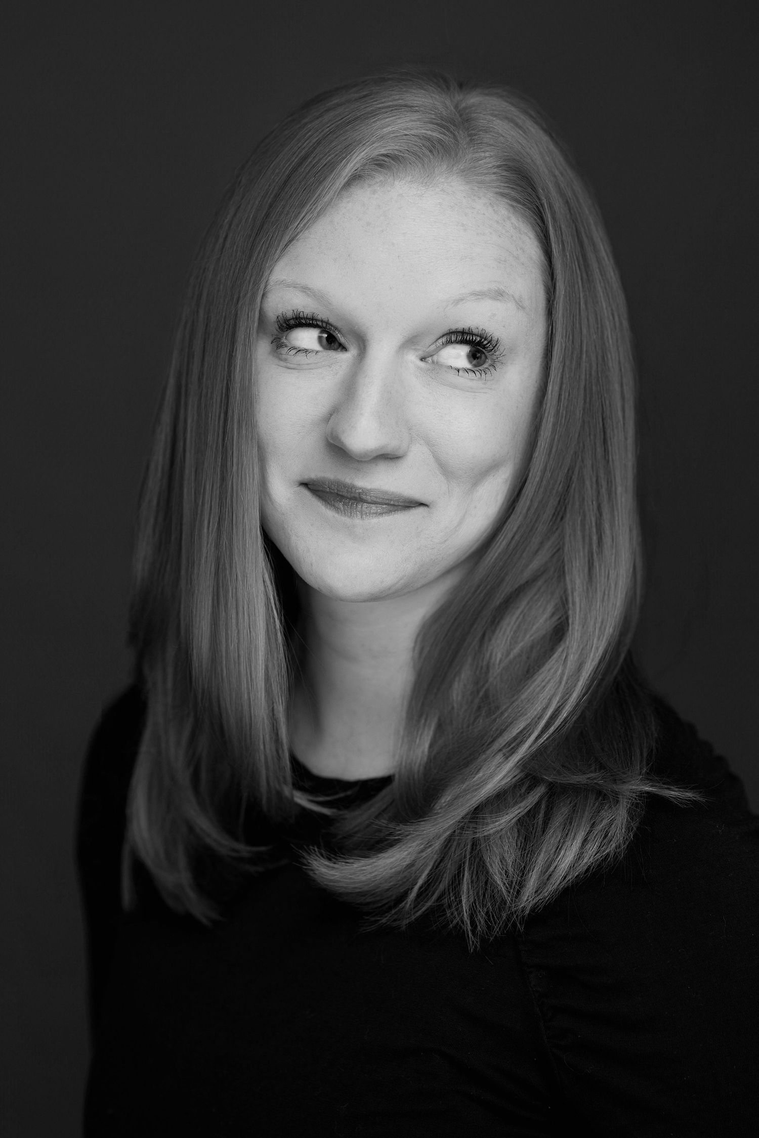 Professional black and white headshot portrait with soft lighting against dark background.
