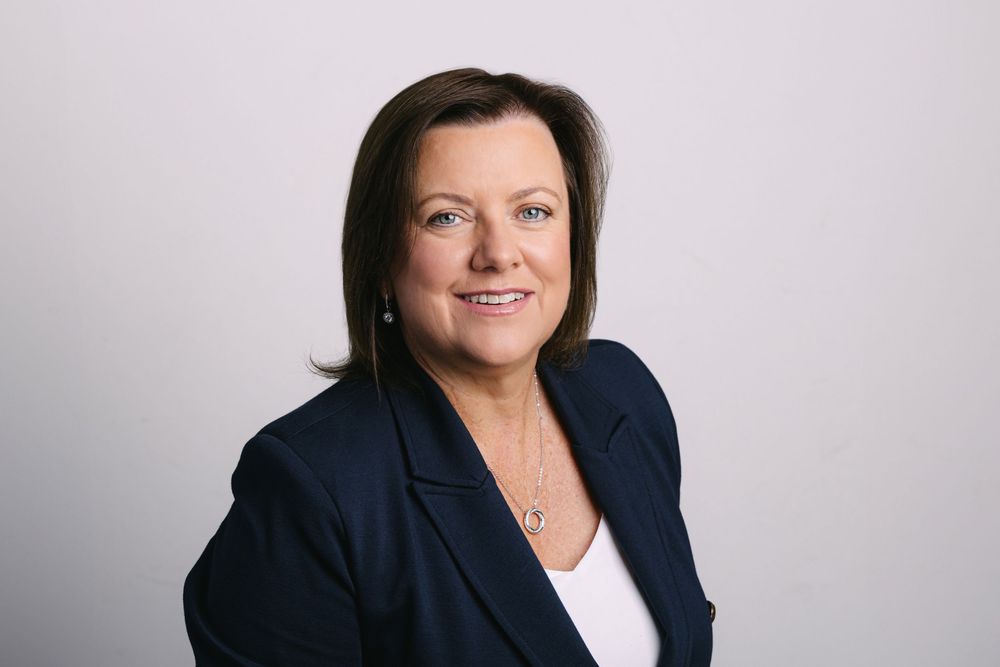 Professional business headshot portrait against light gray background in corporate attire.