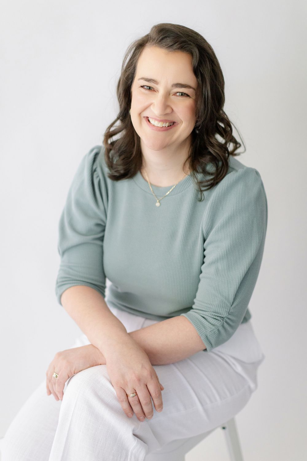 Casual portrait series in sage green top and white pants against light studio background.