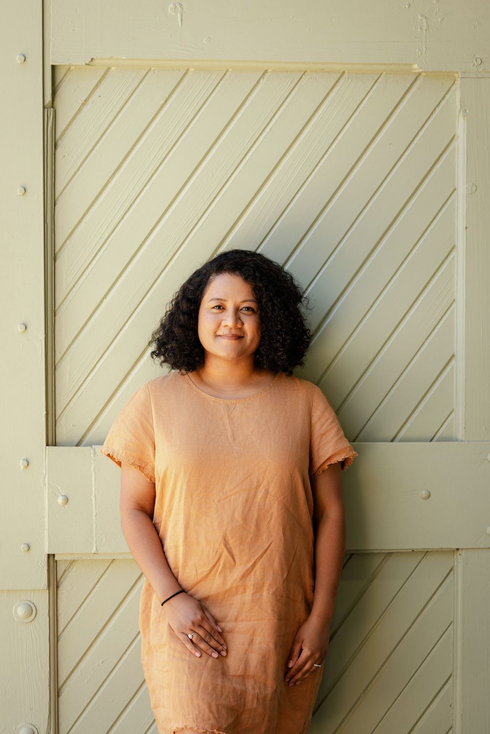 A person in a peach-colored dress stands against a diagonal striped wall background.