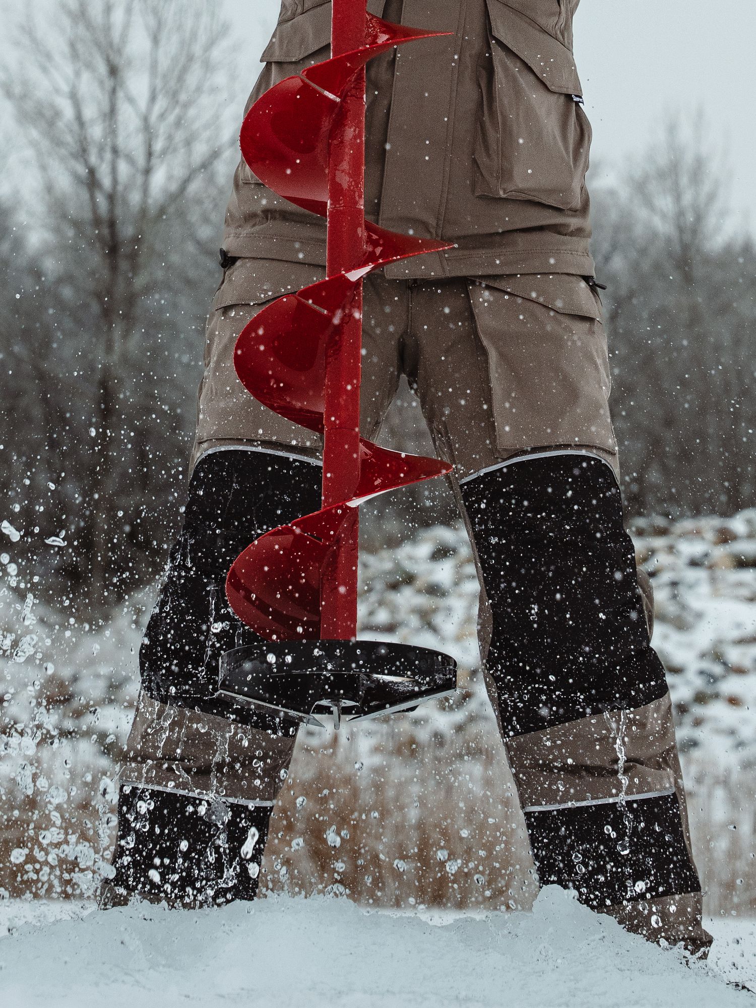 Close-up of red ice auger drilling through snow and ice during winter fishing.
