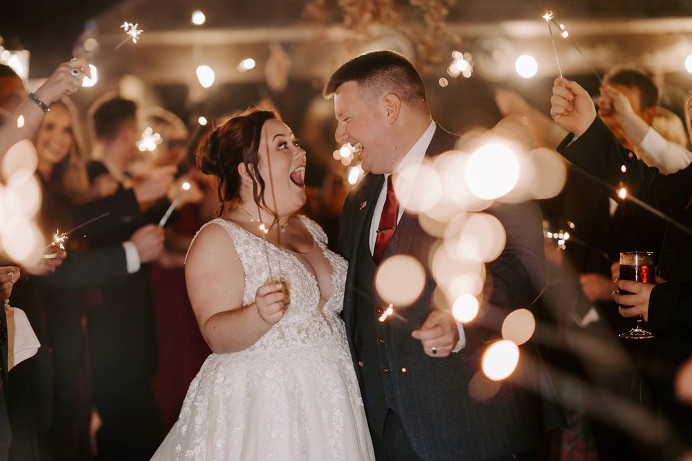 A couple dances together during their wedding reception while guests surround them with glowing sparklers.