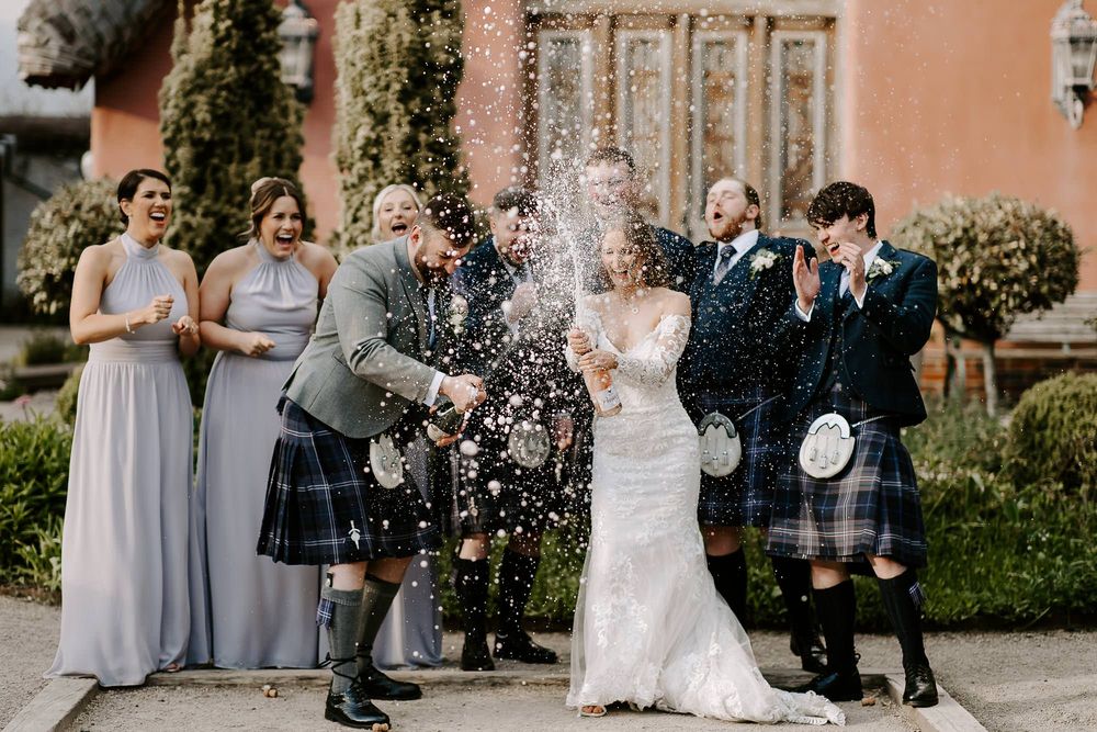 Wedding celebration at a grand venue with champagne spray and guests in traditional Scottish kilts and formal attire.
