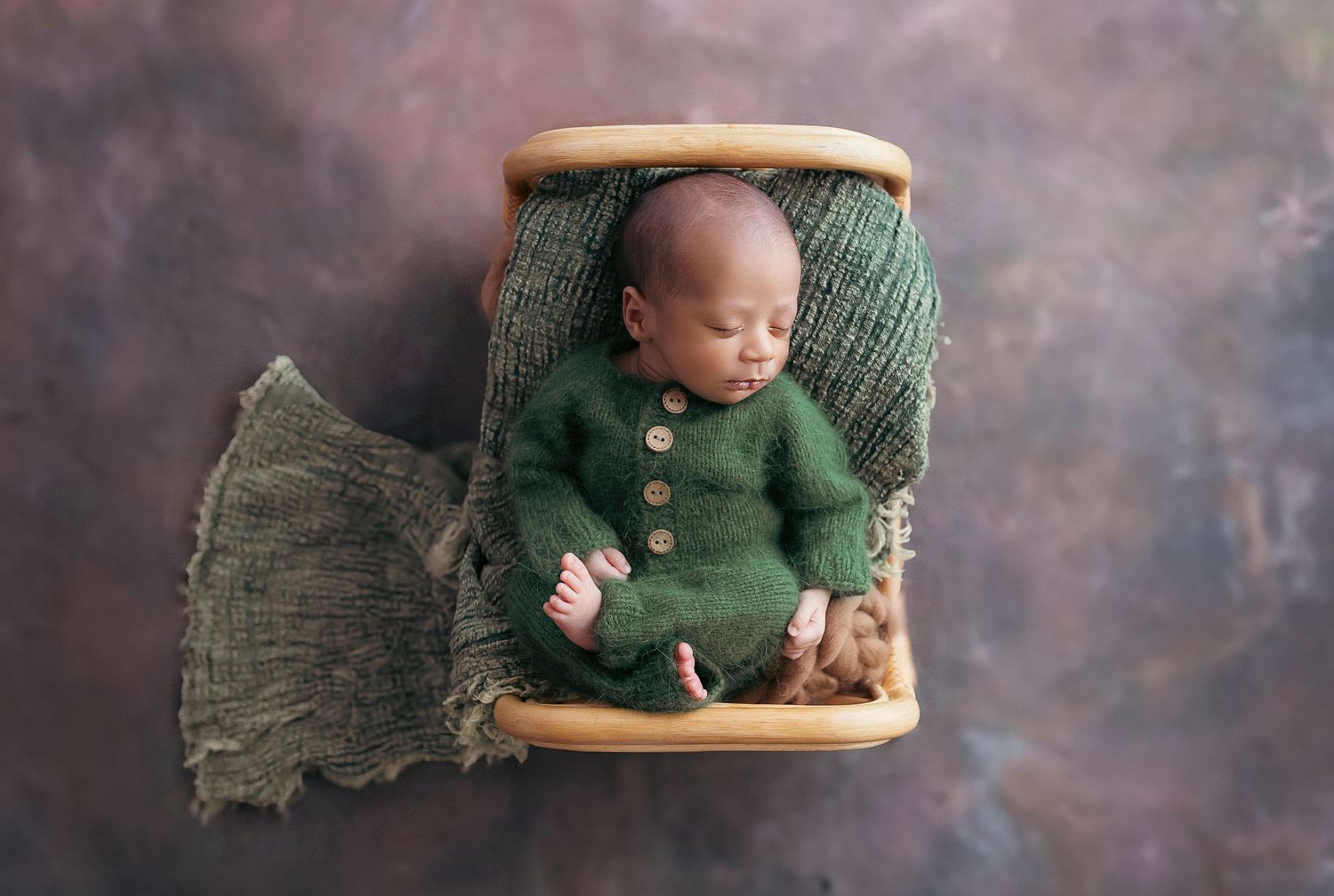 bebe vestido de verde duerme en una camita de ratan boca arriba