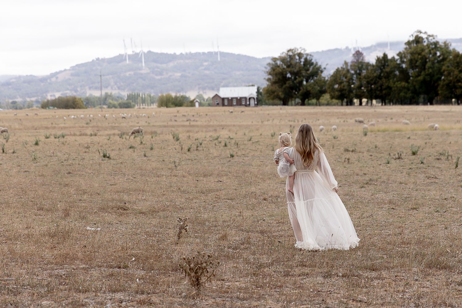 Mum to be walking away with toddler on her hip  during a professional maternity photo shoot.