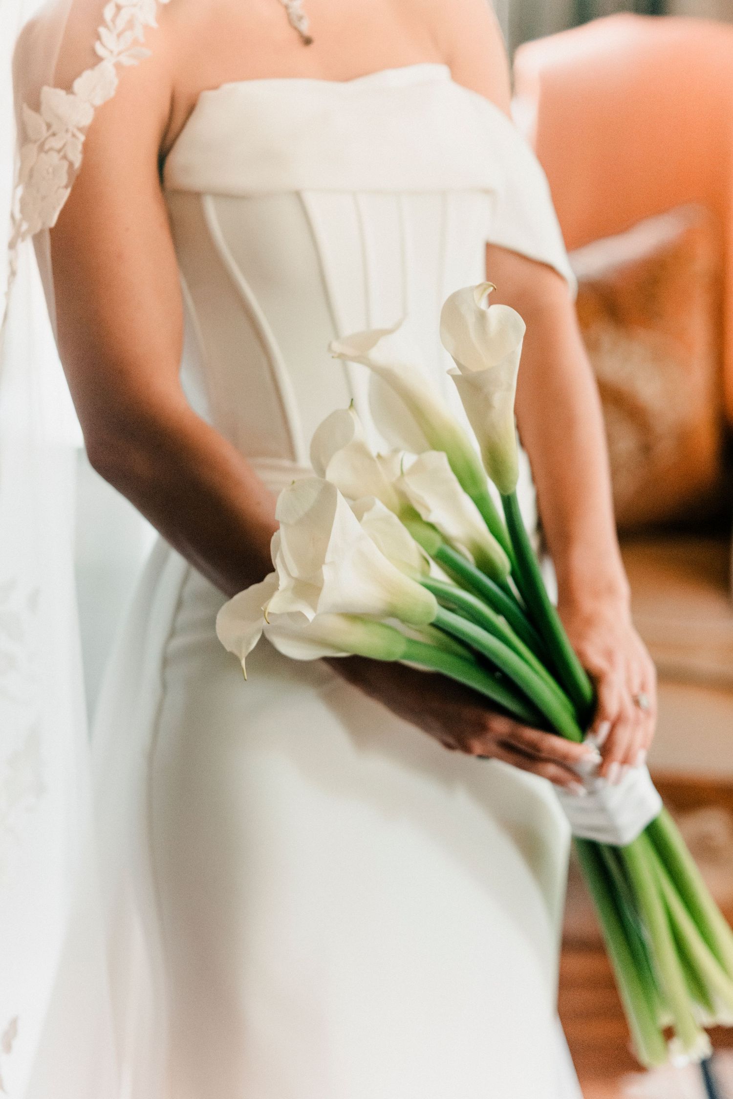 Bride in strapless white corset gown holding minimalist white calla lily bouquet.