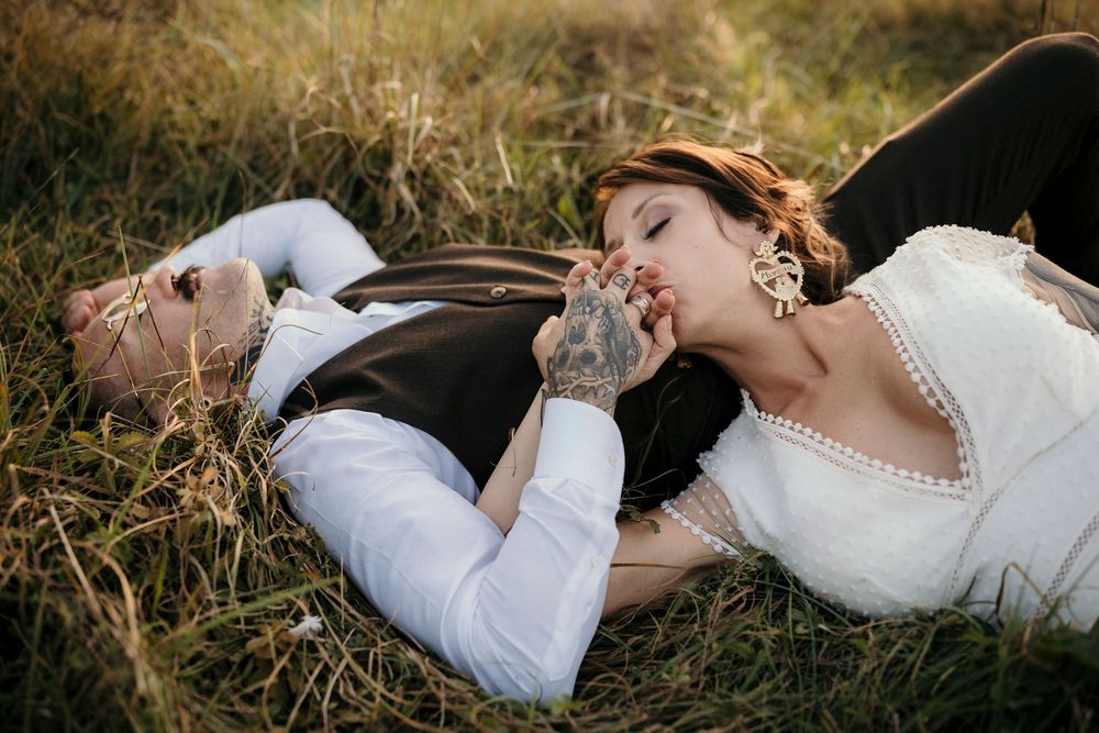 Couple in wedding attire lying together in golden sunlit grass during romantic outdoor photo session.
