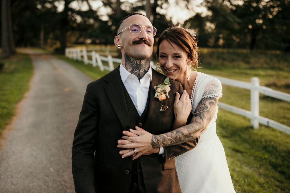 Wedding couple sharing intimate moments along white fence pathway during sunset photo session.