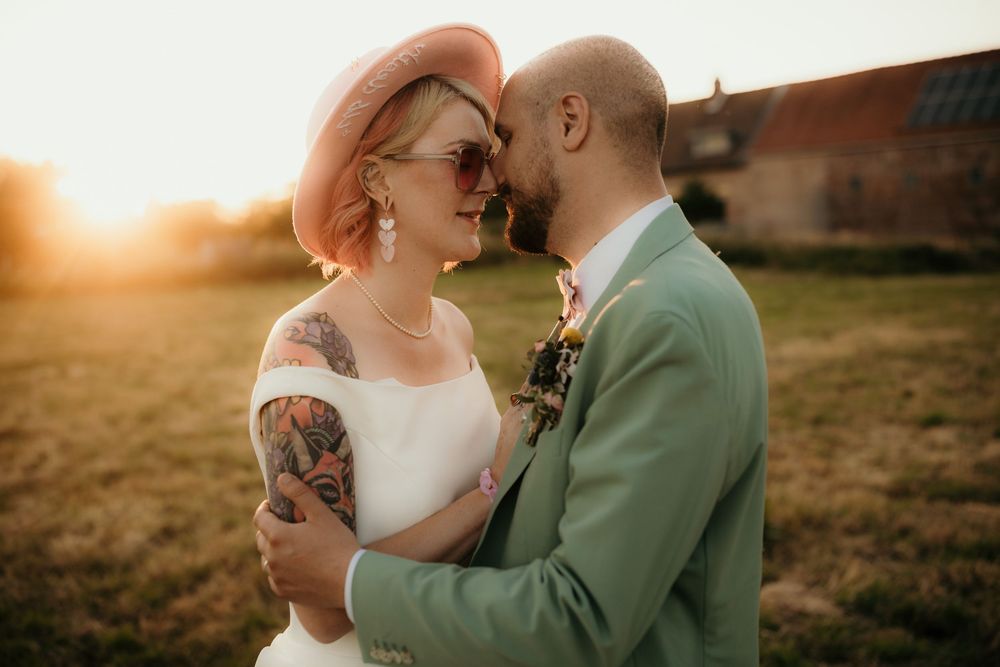 A romantic couple embraces in a golden sunlit field during sunset while wearing wedding attire.