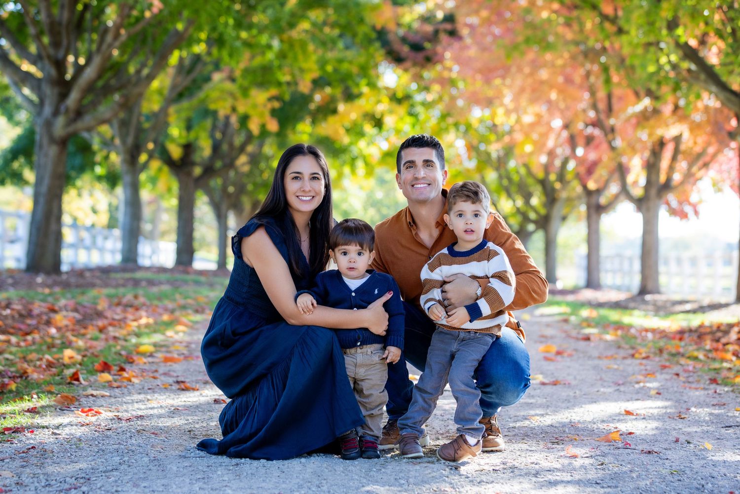 Family sitting together on fallen autumn leaves in a park on a sunny day.