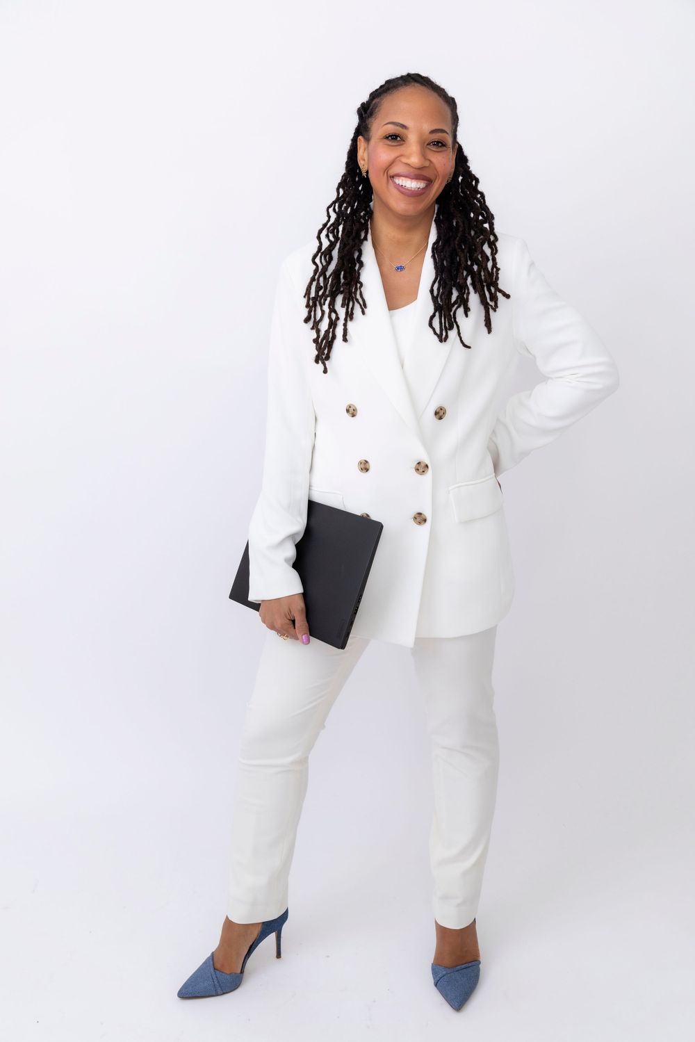 Professional wearing a crisp white power suit with blue heels while holding a black portfolio against white background.