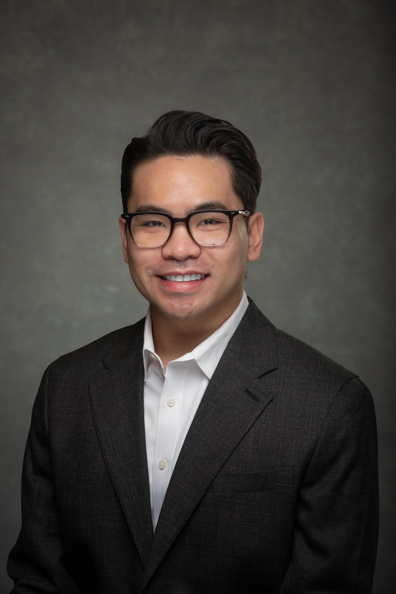 Professional Headshot of Asian man with glasses and dark suit jacket taken in Collierville photography studio.