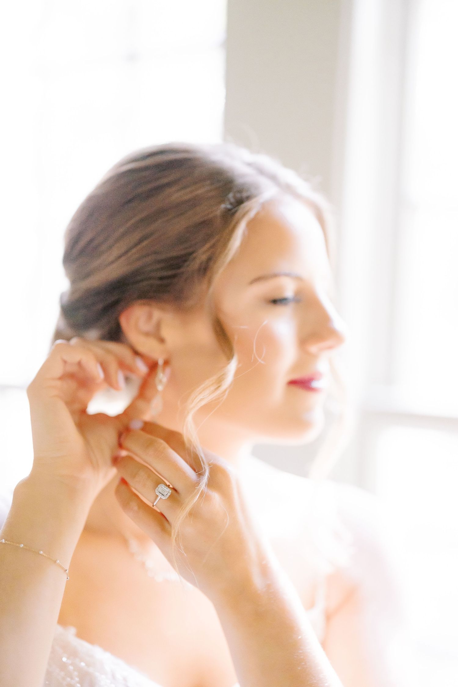 Elegant bride in white lace gown poses in bright sunlit room with bouquet for bridal portrait series.