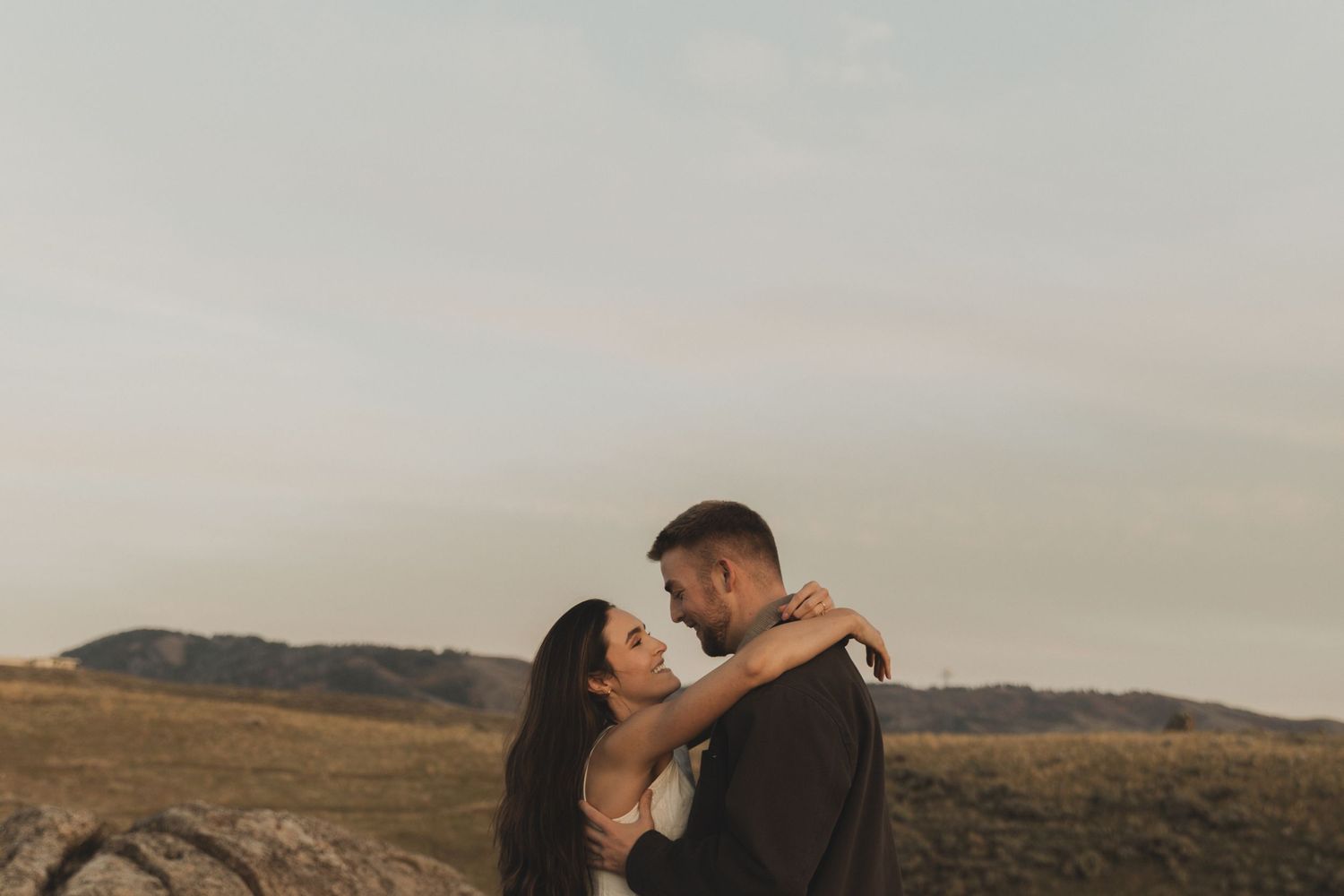 Couple embraces in a romantic moment against a scenic mountain landscape at sunset.