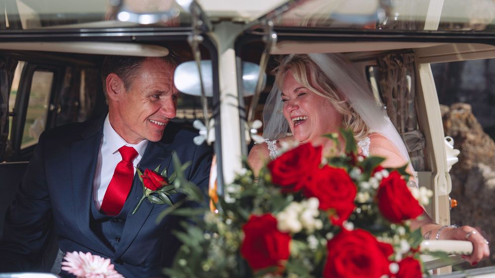 A happy couple shares a joyful moment in their wedding car decorated with red roses.