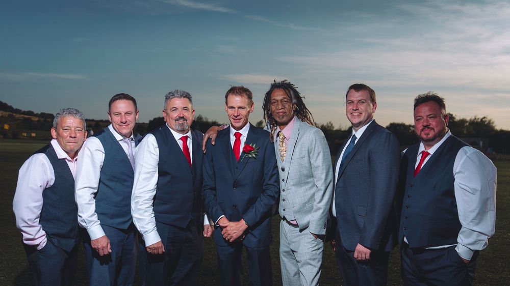 A panoramic view of a wedding party posing together outdoors at sunset with warm lighting and formal attire.