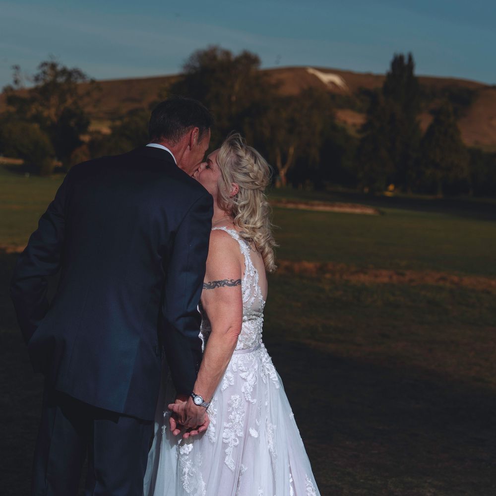 A romantic wedding couple walks together through a scenic outdoor field at sunset, their silhouettes casting long shadows.