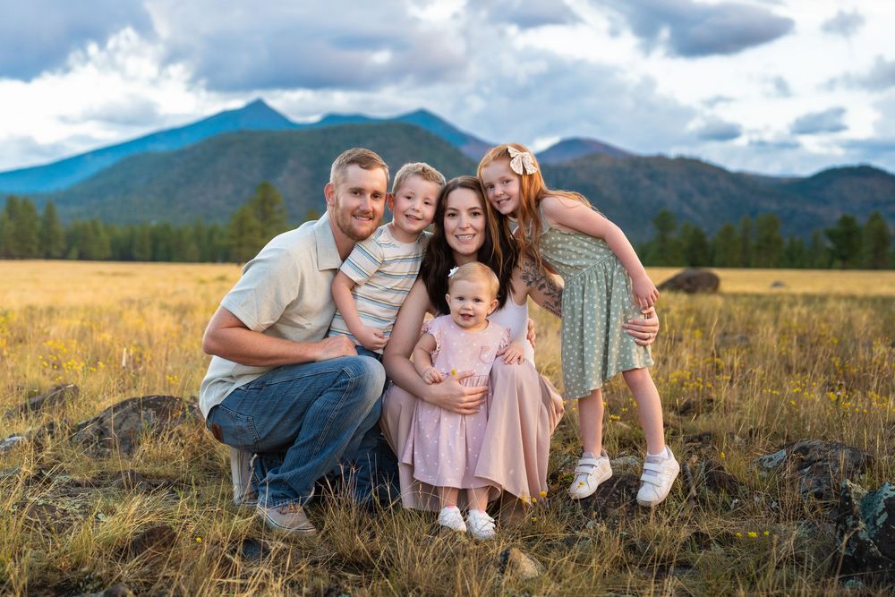 Family poses together in a meadow with mountain peaks and dramatic clouds in the background.