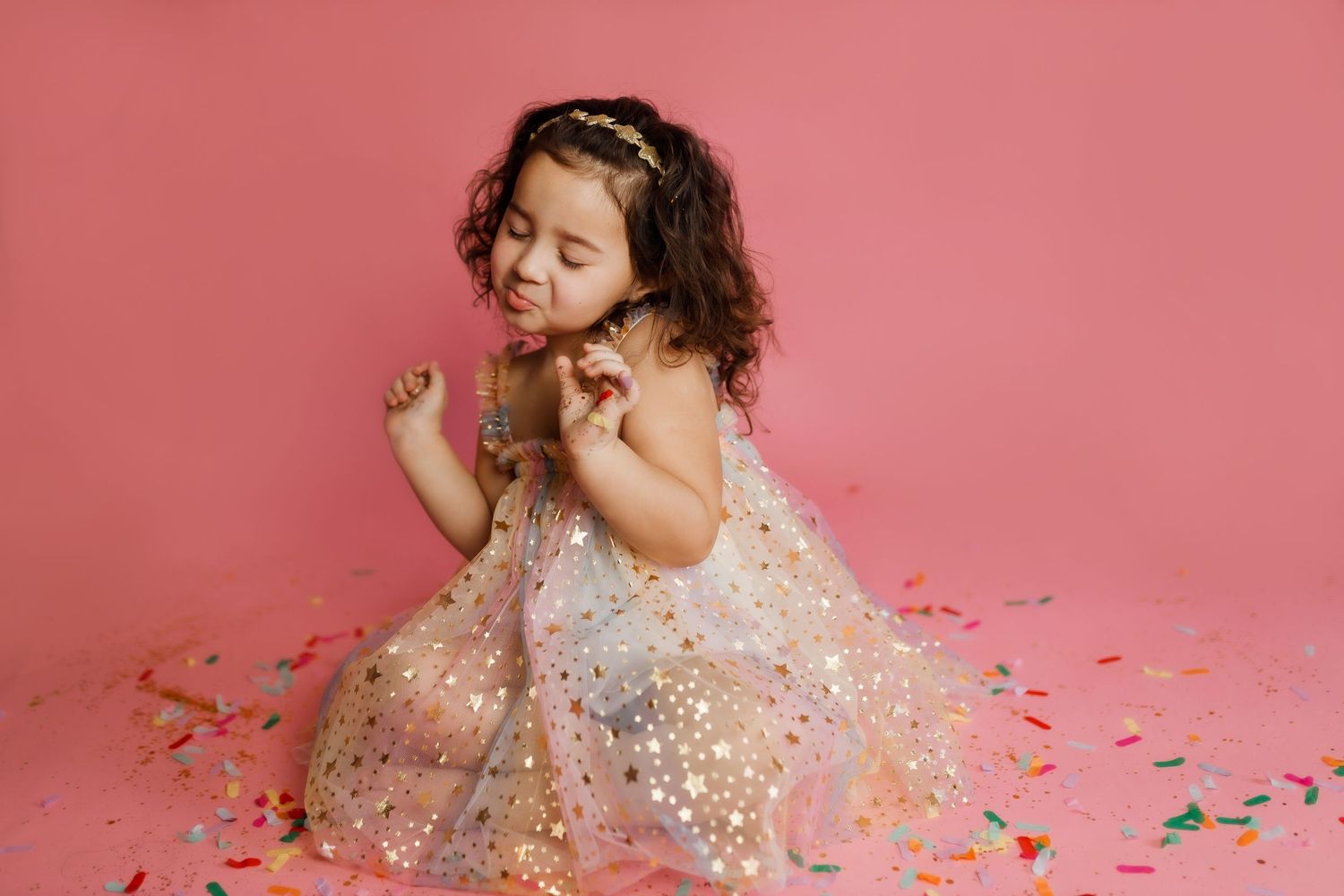 Person in pink dress twirls and dances with glitter confetti against a pink background in a joyful celebration.