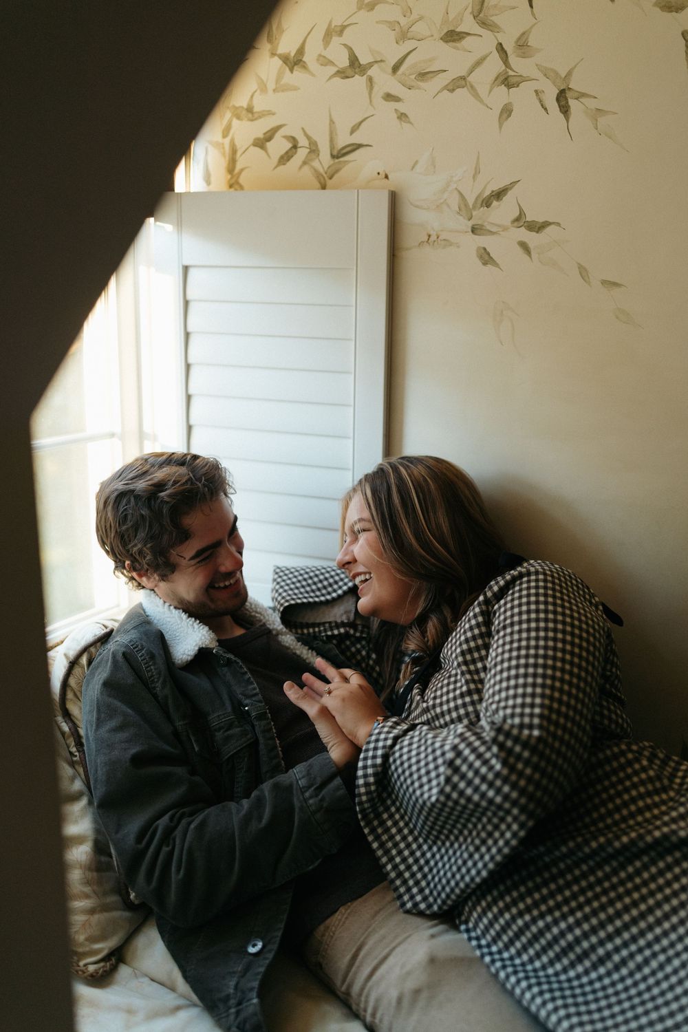 A couple shares tender moments while lying together against a wall in soft indoor lighting.